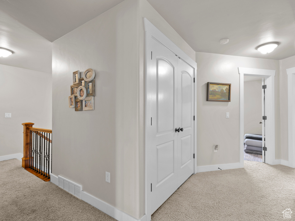 Hallway with light carpet, baseboards, visible vents, and an upstairs landing