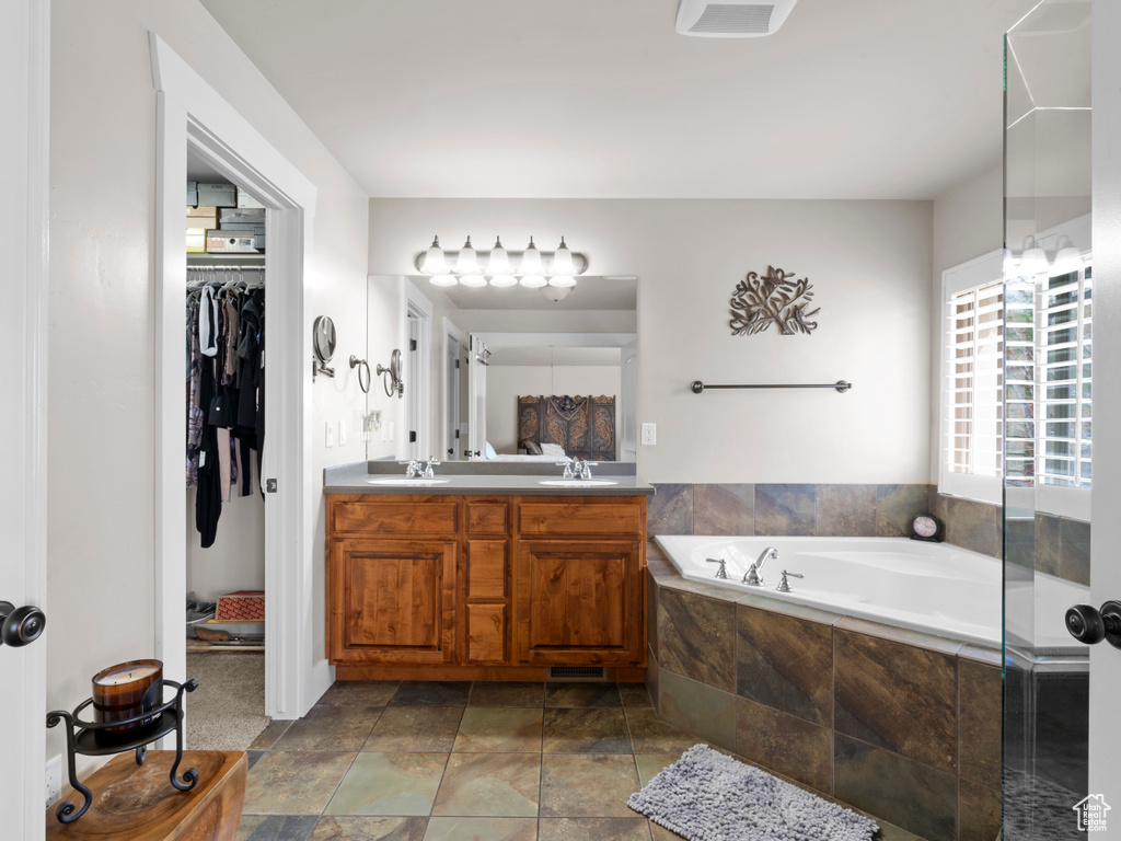 Bathroom featuring a sink, a bath, a spacious closet, double vanity, and stone finish flooring