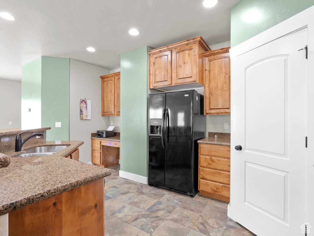 Kitchen with a sink, black fridge with ice dispenser, light stone countertops, stone finish floor, and recessed lighting
