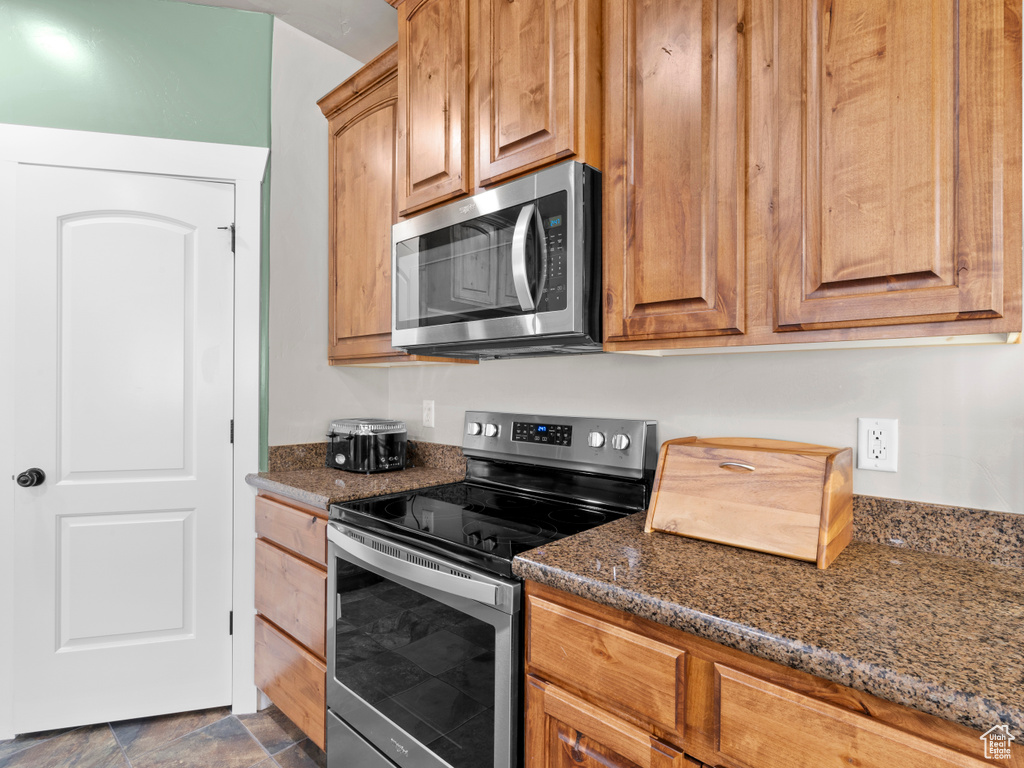 Kitchen with stainless steel appliances, stone finish floor, and dark stone counters