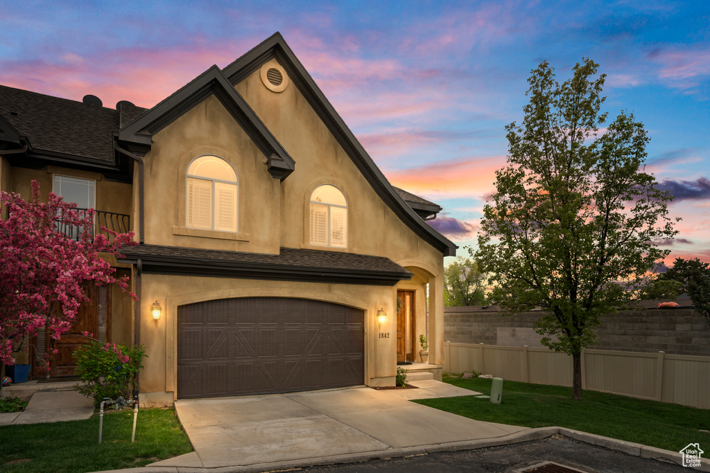 View of front of property featuring concrete driveway, fence, a garage, a lawn, and stucco siding