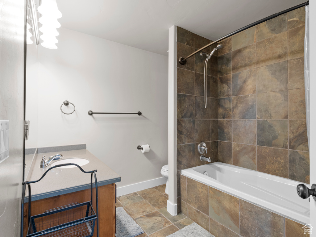 Bathroom with tiled shower / bath, vanity, stone tile flooring, baseboards, and toilet