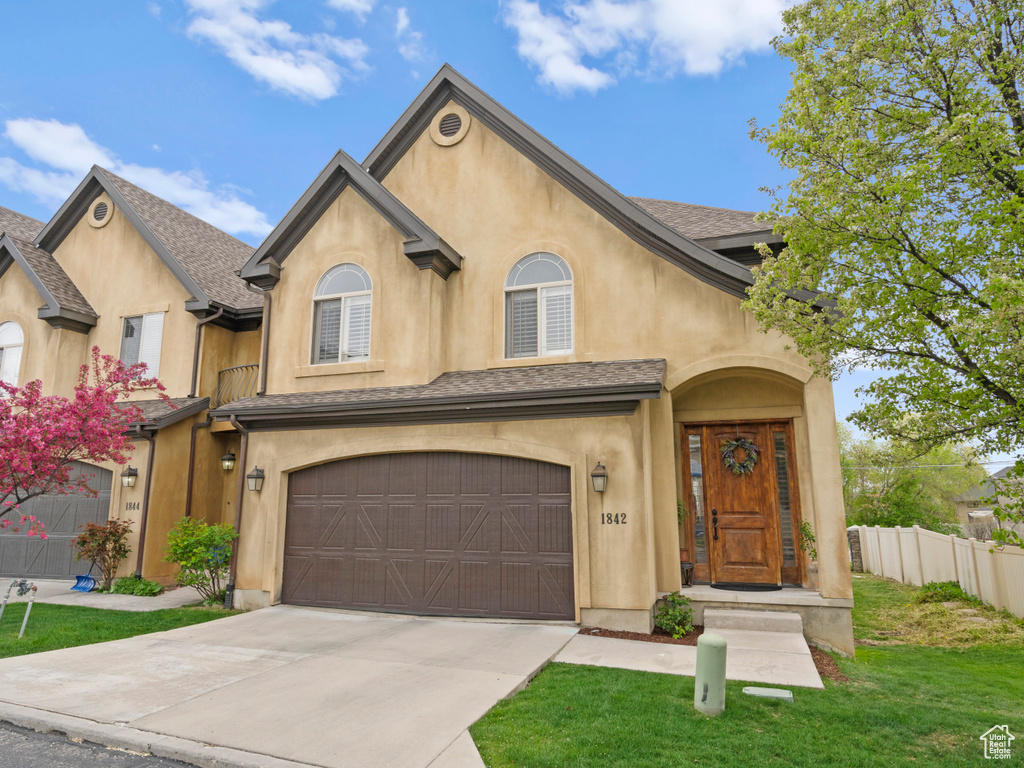 View of front of home with a garage, driveway, fence, a front yard, and stucco siding