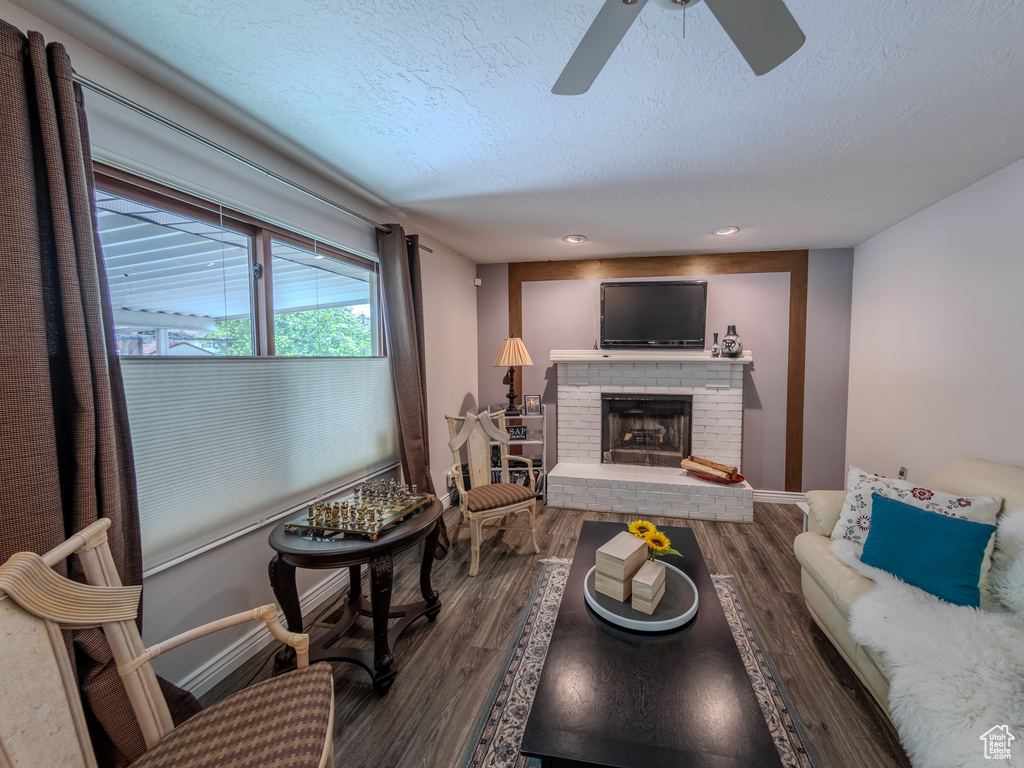 Living area featuring a ceiling fan, a textured ceiling, a brick fireplace, and wood finished floors