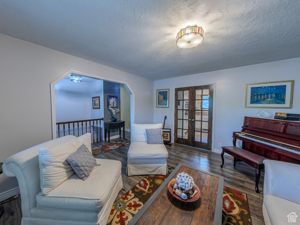 Living room with arched walkways, a textured ceiling, french doors, baseboards, and wood finished floors