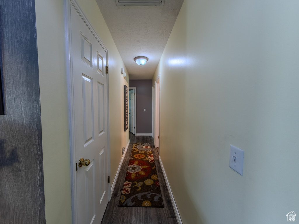 Corridor with a textured ceiling, baseboards, visible vents, and wood finished floors