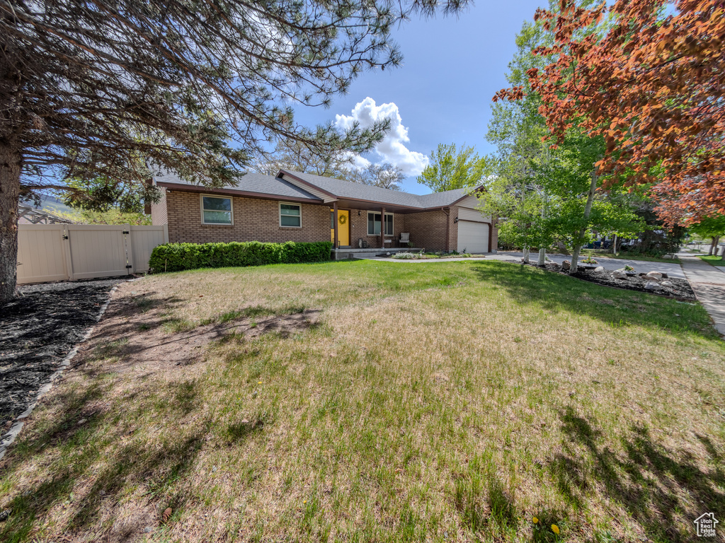 Ranch-style home featuring an attached garage, a gate, brick siding, and a front yard