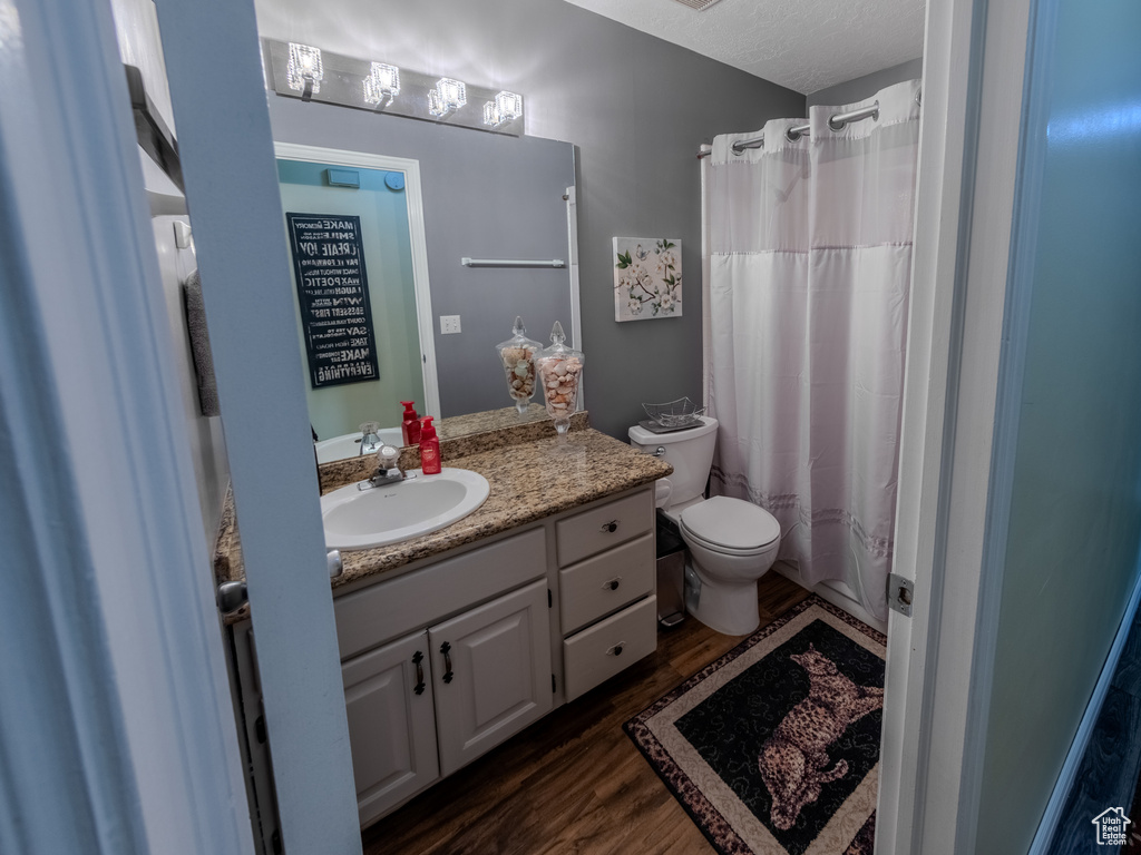 Full bathroom with toilet, a shower with curtain, wood finished floors, and vanity