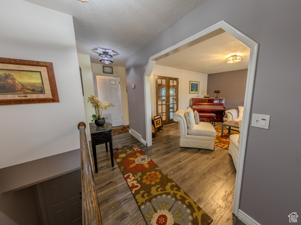 Hall featuring french doors, a textured ceiling, baseboards, and wood finished floors