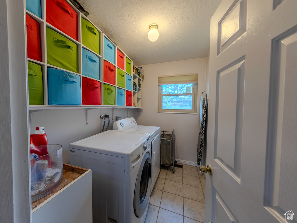 Laundry area with independent washer and dryer, a textured ceiling, laundry area, and light tile patterned floors