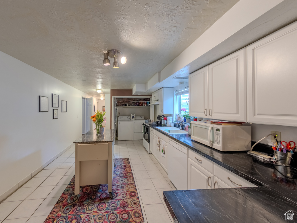 Kitchen featuring a sink, light tile patterned floors, white cabinets, white appliances, and washer and clothes dryer