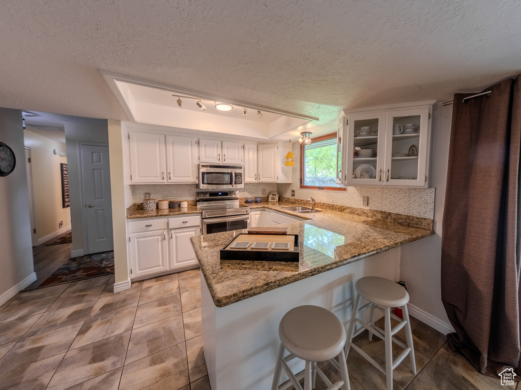 Kitchen featuring a peninsula, baseboards, a textured ceiling, white cabinetry, and appliances with stainless steel finishes