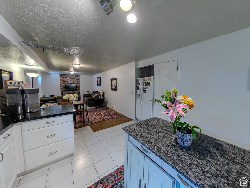 Kitchen featuring white fridge with ice dispenser, dark stone countertops, white cabinetry, open floor plan, and light tile patterned floors