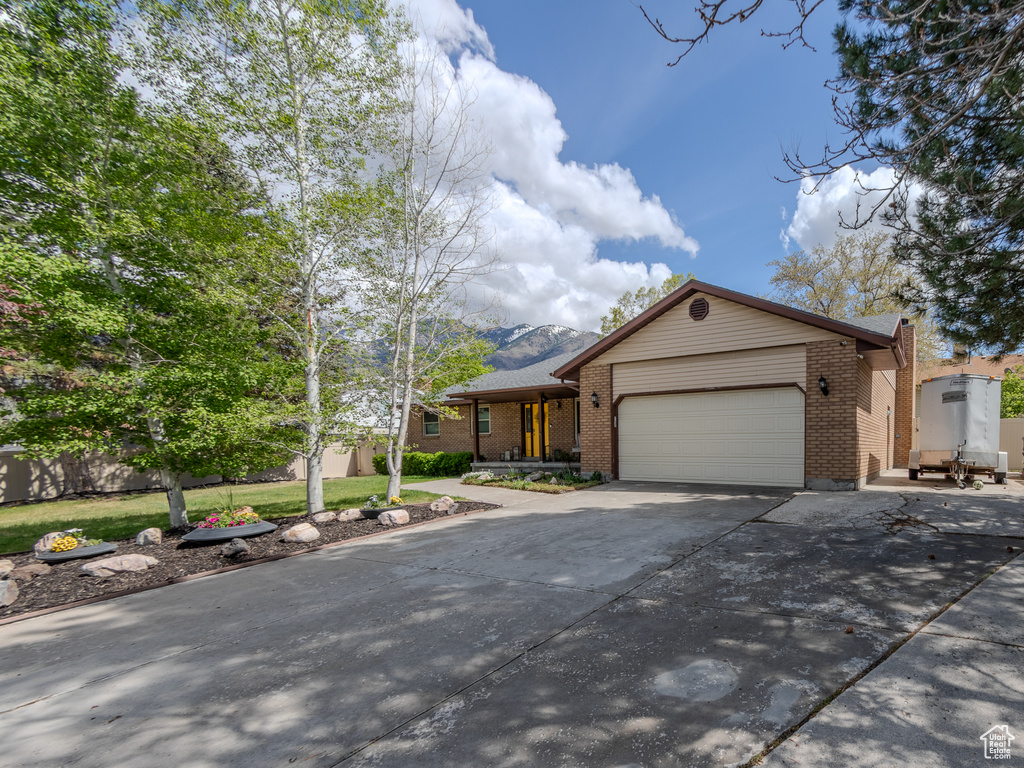 Ranch-style house with driveway, brick siding, a mountain view, a front lawn, and an attached garage