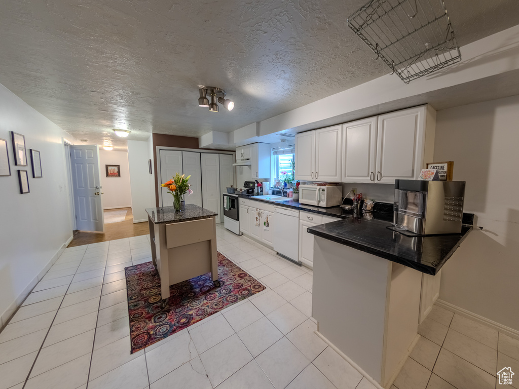 Kitchen with a peninsula, light tile patterned floors, white cabinets, and white appliances
