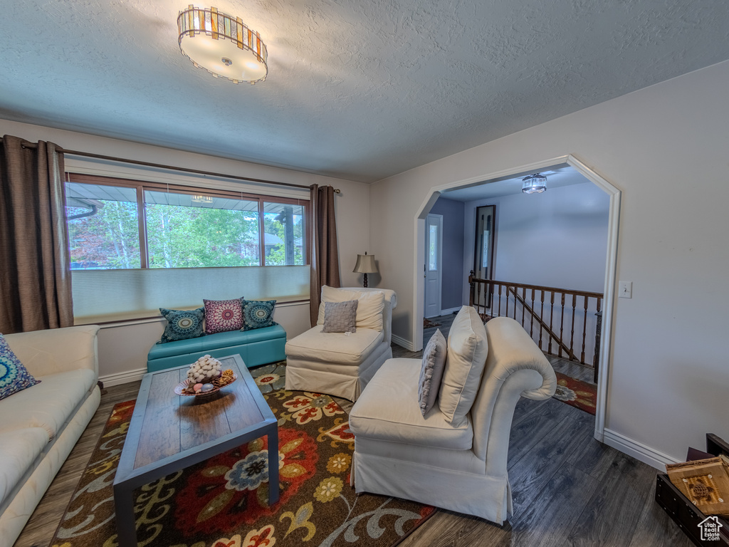 Living room with baseboards, a textured ceiling, arched walkways, and wood finished floors