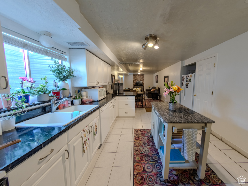 Kitchen with light tile patterned flooring, a sink, white appliances, white cabinetry, and visible vents