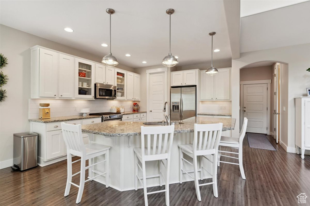 Kitchen with appliances with stainless steel finishes, a sink, arched walkways, white cabinetry, and backsplash