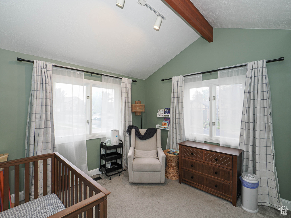Bedroom with carpet flooring, baseboards, lofted ceiling with beams, and a crib