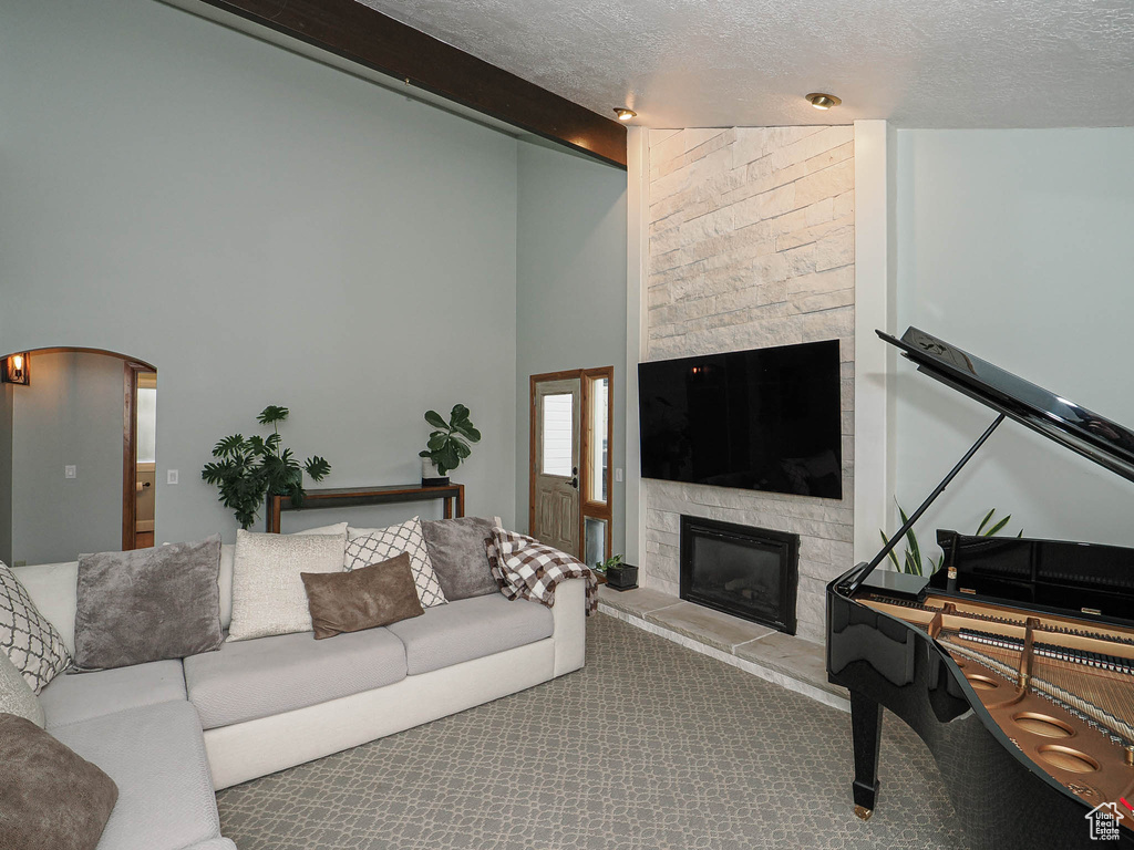 Living area with beam ceiling, a stone fireplace, a textured ceiling, arched walkways, and carpet