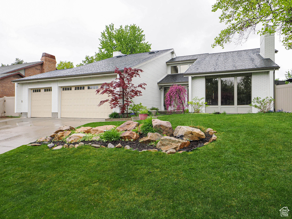 Ranch-style house featuring an attached garage, brick siding, a front yard, a chimney, and driveway