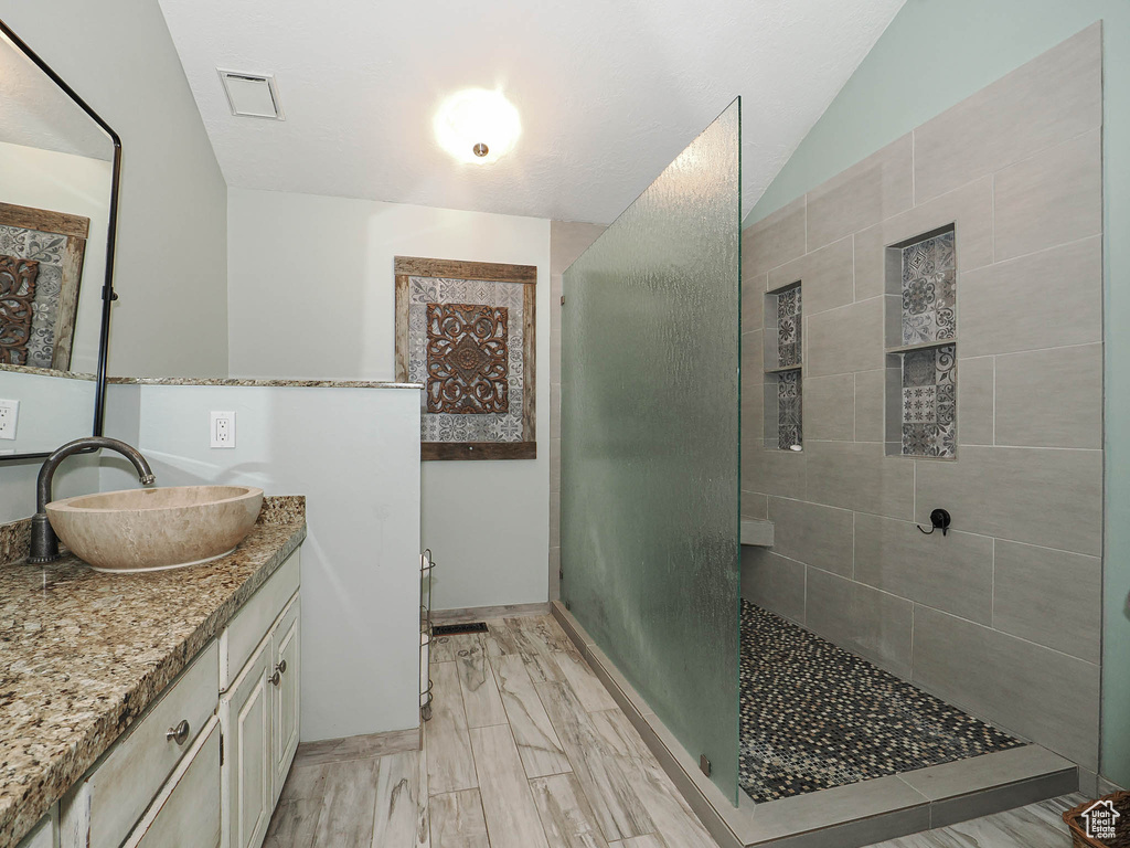 Bathroom featuring vaulted ceiling, vanity, a tile shower, and visible vents