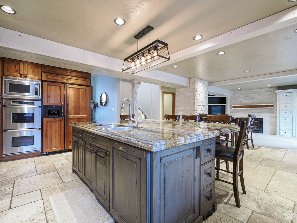 Kitchen with a sink, built in appliances, decorative columns, and stone tile flooring