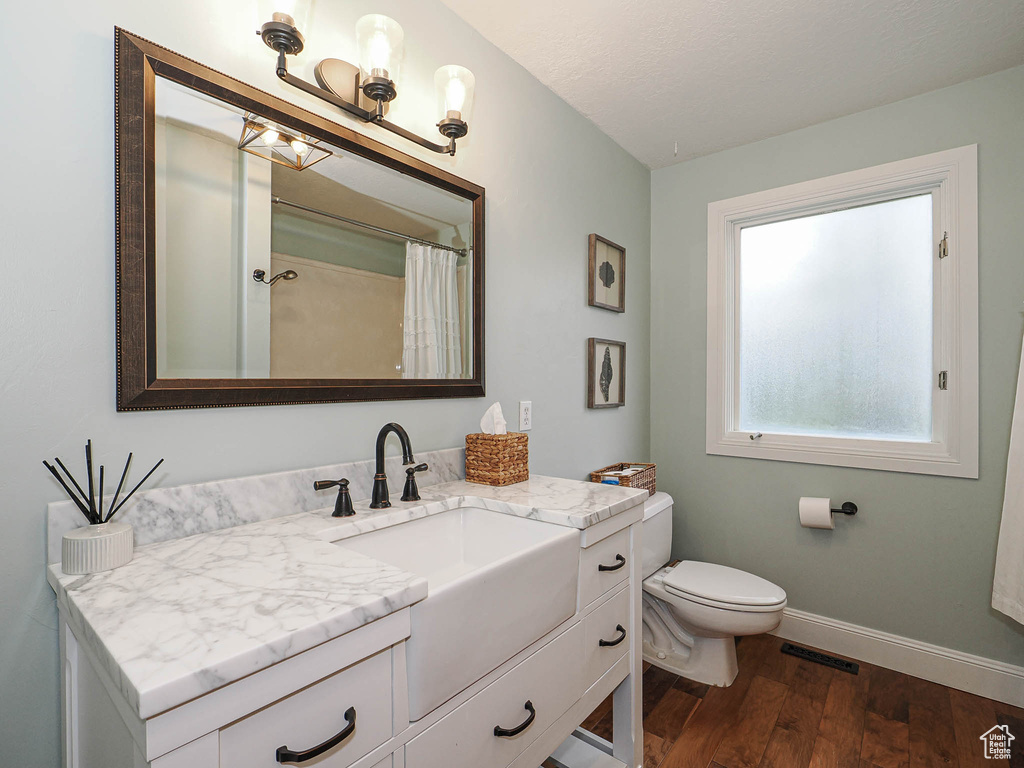 Full bath with vanity, toilet, baseboards, wood finished floors, and visible vents