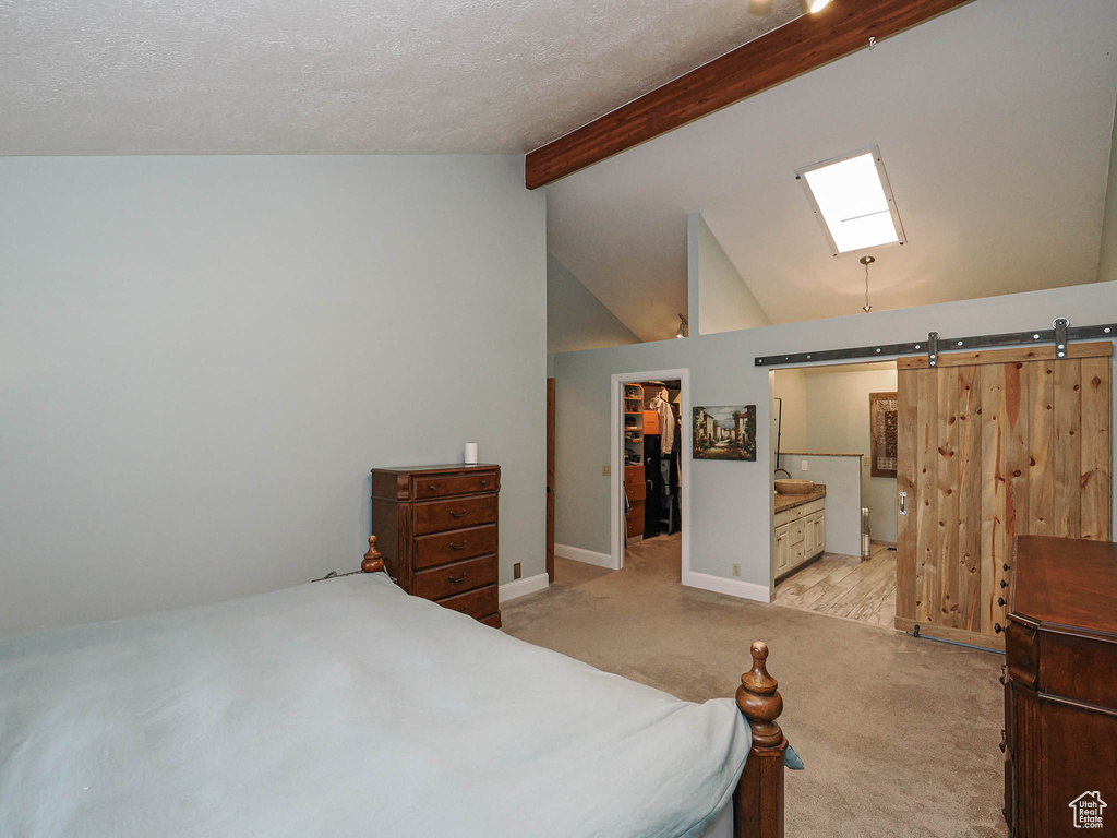 Carpeted bedroom with a barn door, a walk in closet, high vaulted ceiling, baseboards, and beamed ceiling