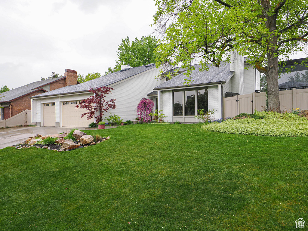 View of front of property featuring a garage, fence, a front yard, brick siding, and concrete driveway