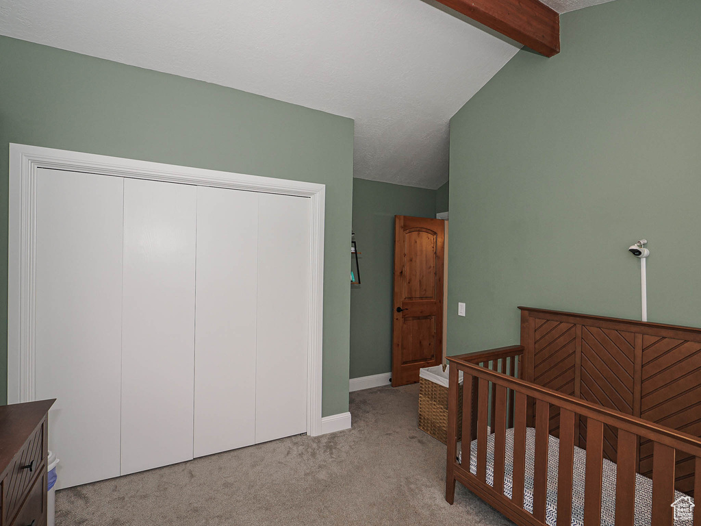Bedroom featuring carpet floors, vaulted ceiling with beams, baseboards, and a closet