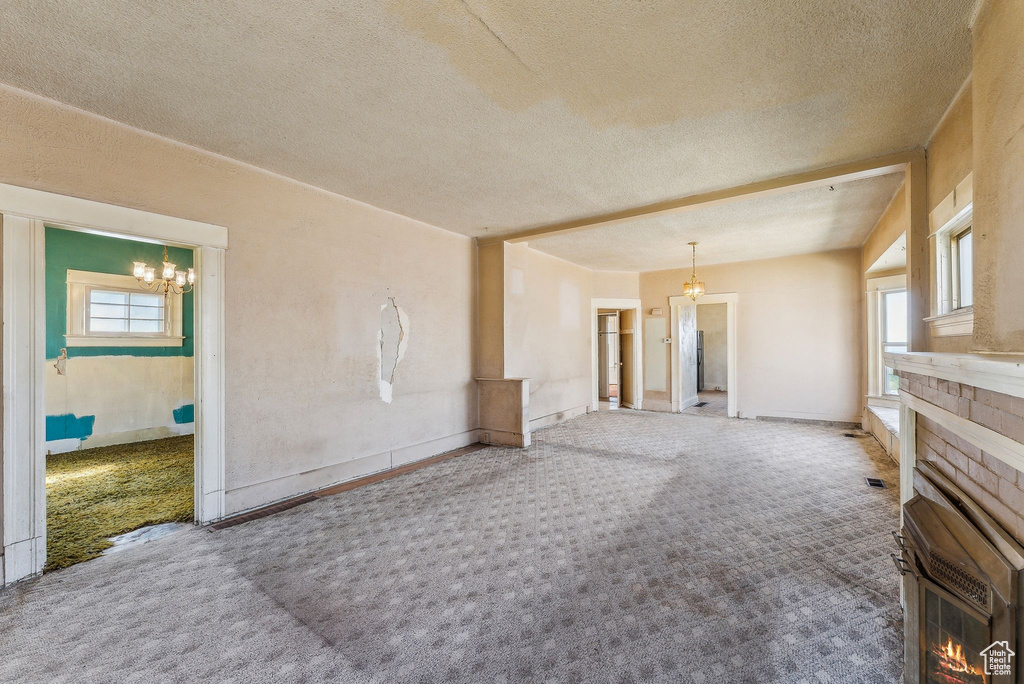 Unfurnished living room with carpet floors, a textured ceiling, a notable chandelier, and a fireplace