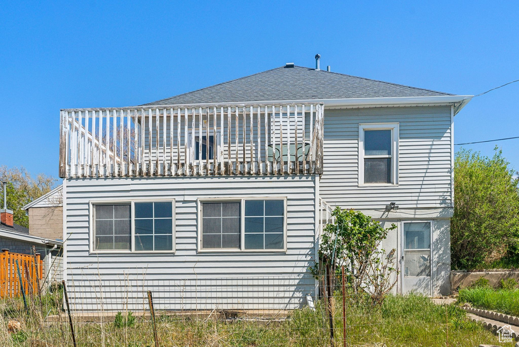 Back of property with a shingled roof, fence, and a balcony