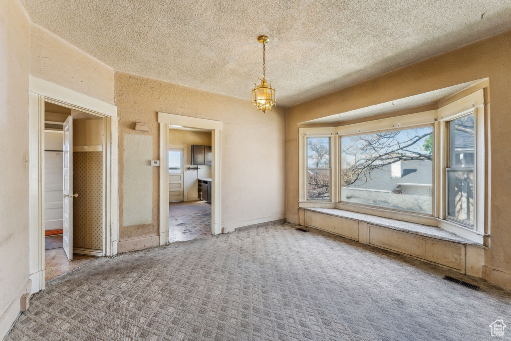 Unfurnished dining area featuring visible vents, a textured ceiling, carpet floors, and an inviting chandelier