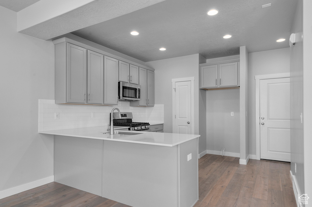 Kitchen featuring a peninsula, baseboards, gray cabinets, appliances with stainless steel finishes, and backsplash