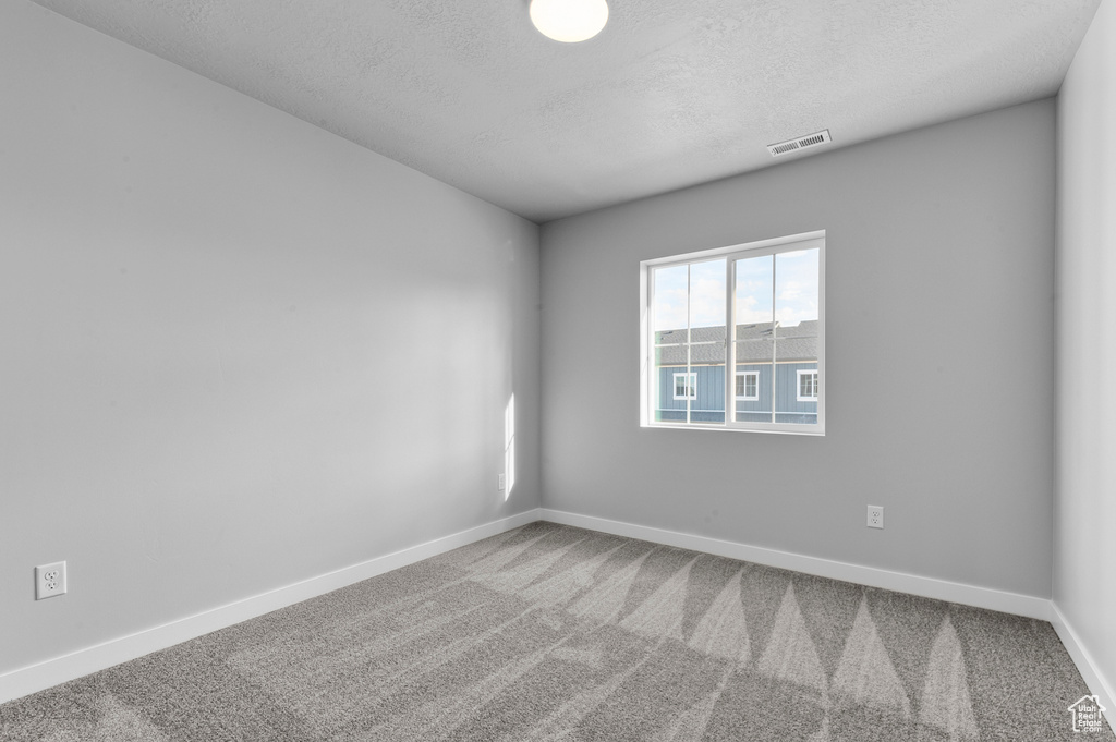 Carpeted empty room featuring a textured ceiling, visible vents, and baseboards