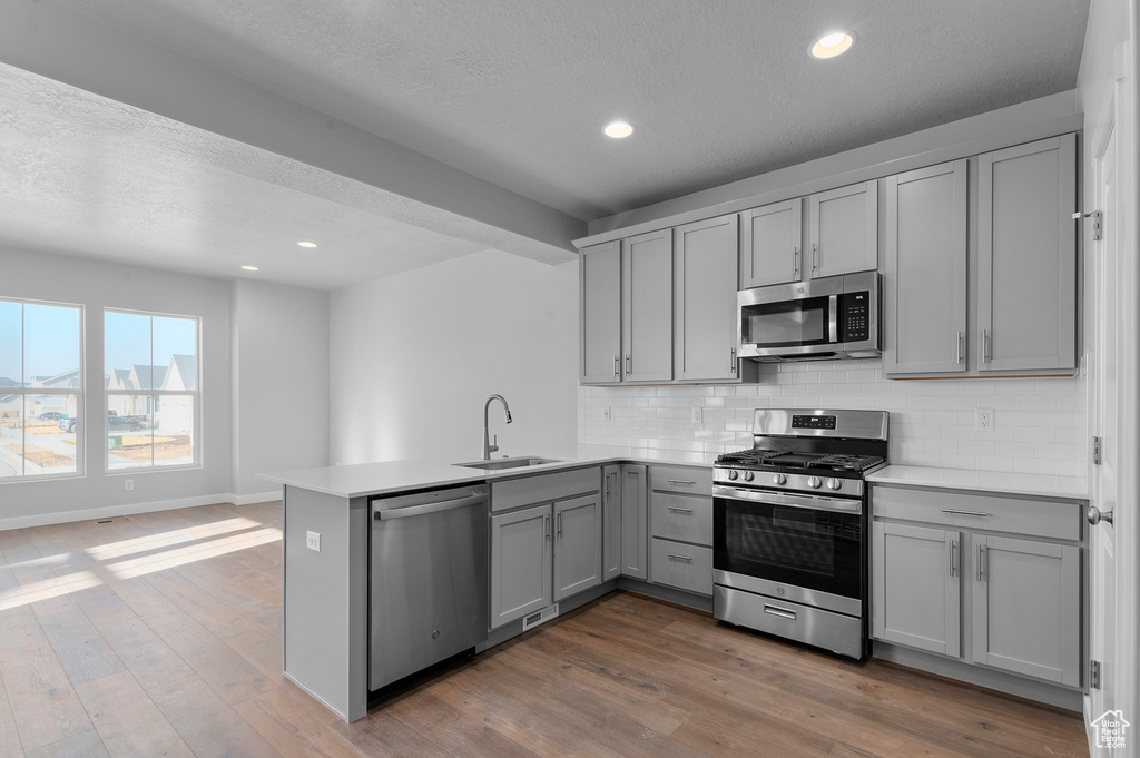 Kitchen with a peninsula, gray cabinets, a sink, backsplash, and stainless steel appliances