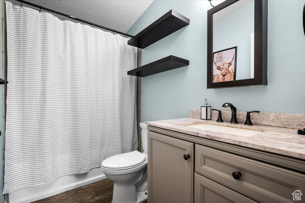 Bathroom with vanity, wood finished floors, toilet, shower / bathtub combination with curtain, and a textured ceiling