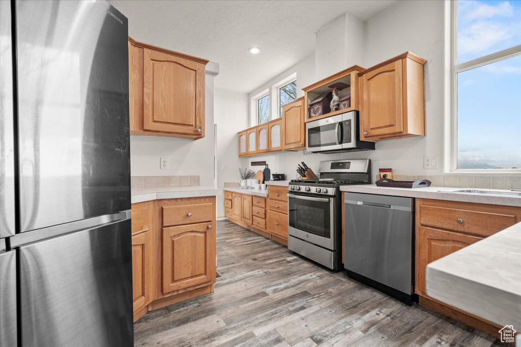 Kitchen with open shelves, light countertops, stainless steel appliances, recessed lighting, and light wood-type flooring