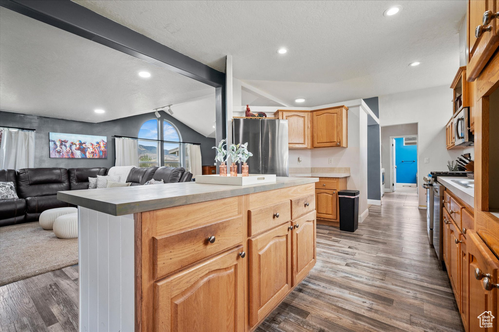 Kitchen with stainless steel appliances, open floor plan, wood finished floors, a kitchen island, and vaulted ceiling
