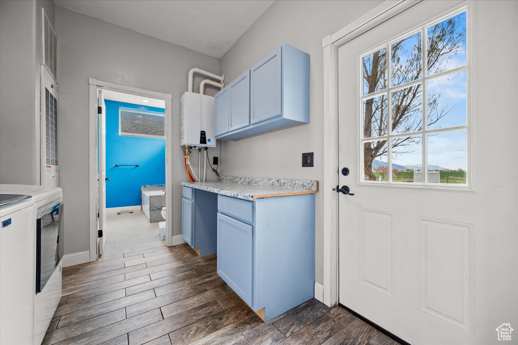 Clothes washing area with cabinet space, dark wood-style flooring, washing machine and dryer, and tankless water heater