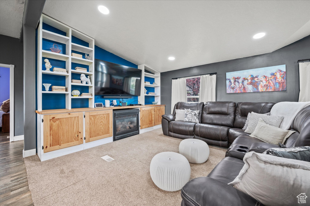 Living area featuring recessed lighting, a glass covered fireplace, wood finished floors, and vaulted ceiling