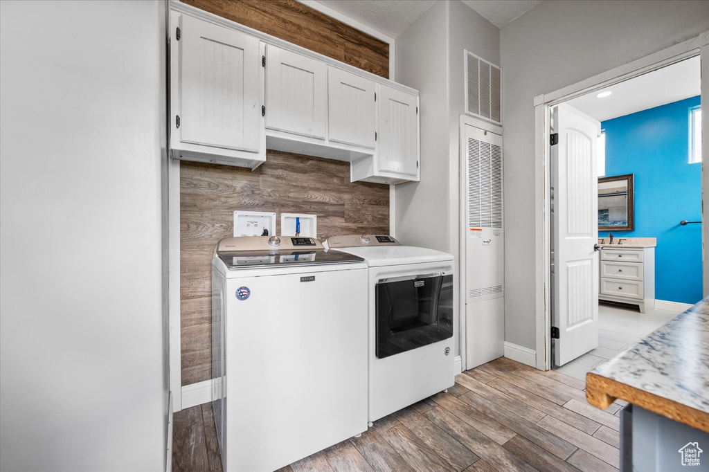 Washroom featuring visible vents, cabinet space, baseboards, light wood finished floors, and washer and dryer