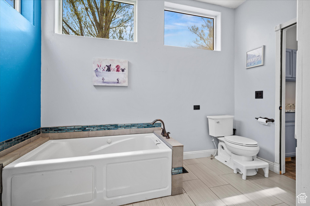 Full bath with toilet, baseboards, plenty of natural light, and a bath