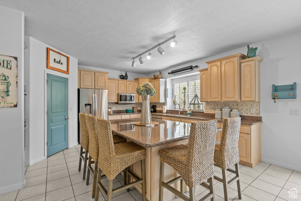 Kitchen with light brown cabinetry, appliances with stainless steel finishes, decorative backsplash, and light tile patterned floors