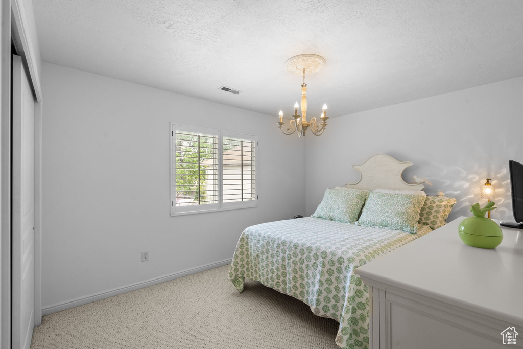 Bedroom featuring light colored carpet, a notable chandelier, a textured ceiling, baseboards, and visible vents