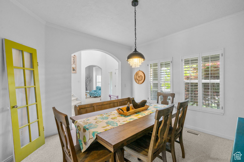 Dining space with crown molding, visible vents, baseboards, light colored carpet, and arched walkways