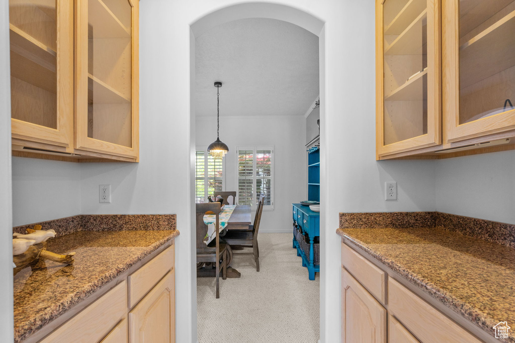 Kitchen featuring arched walkways, light stone counters, glass insert cabinets, light brown cabinets, and light carpet