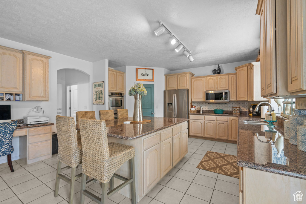 Kitchen featuring a sink, arched walkways, a center island, stainless steel appliances, and light tile patterned floors