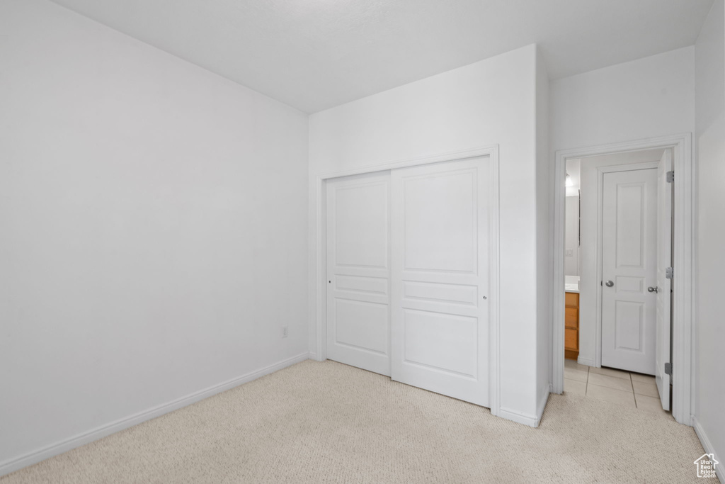 Unfurnished bedroom with baseboards, light carpet, and a closet
